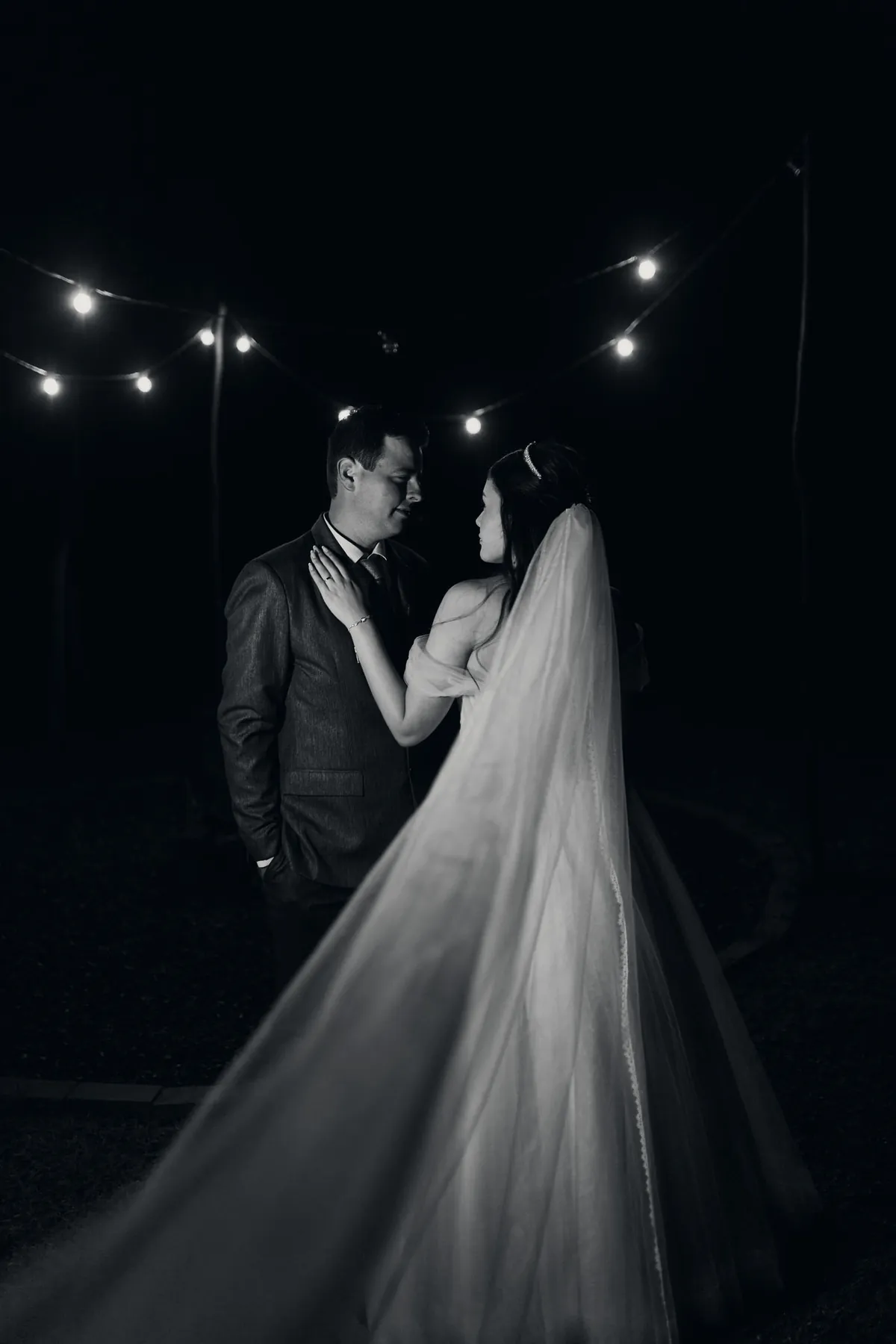 Casal dançando à noite sob luzes, em preto e branco