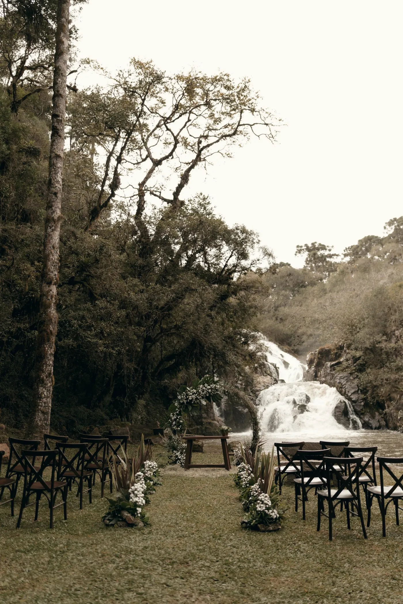 Cadeiras de madeira dispostas para cerimônia diante de uma cascata